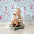Lovely child standing in front of Whimsy Tots Seaside Village Parade Wallpaper in Blue with fish, house, anchor, starfish, bubble in design. Lovely child standing in front of Whimsy Tots Seaside Village Parade Wallpaper in Blue with fish, house, anchor, starfish, bubble in design.