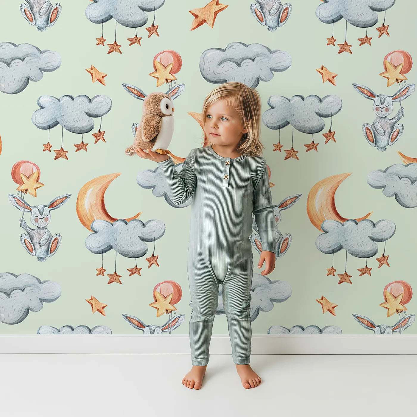 Lovely child standing in front of Whimsy Tots Moonlight Bunny Dreams Wallpaper in Green with rabbit, balloon, moon, star, cloud in design.