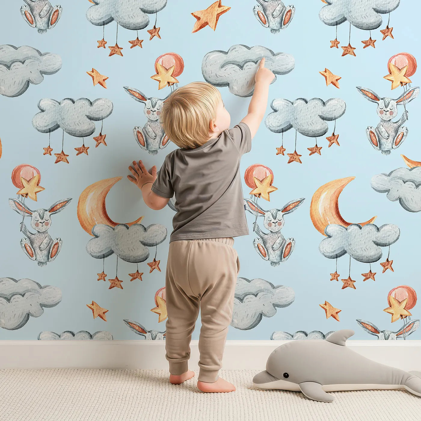 Lovely child standing in front of Whimsy Tots Moonlight Bunny Dreams Wallpaper in Blue with rabbit, balloon, moon, star, cloud in design.