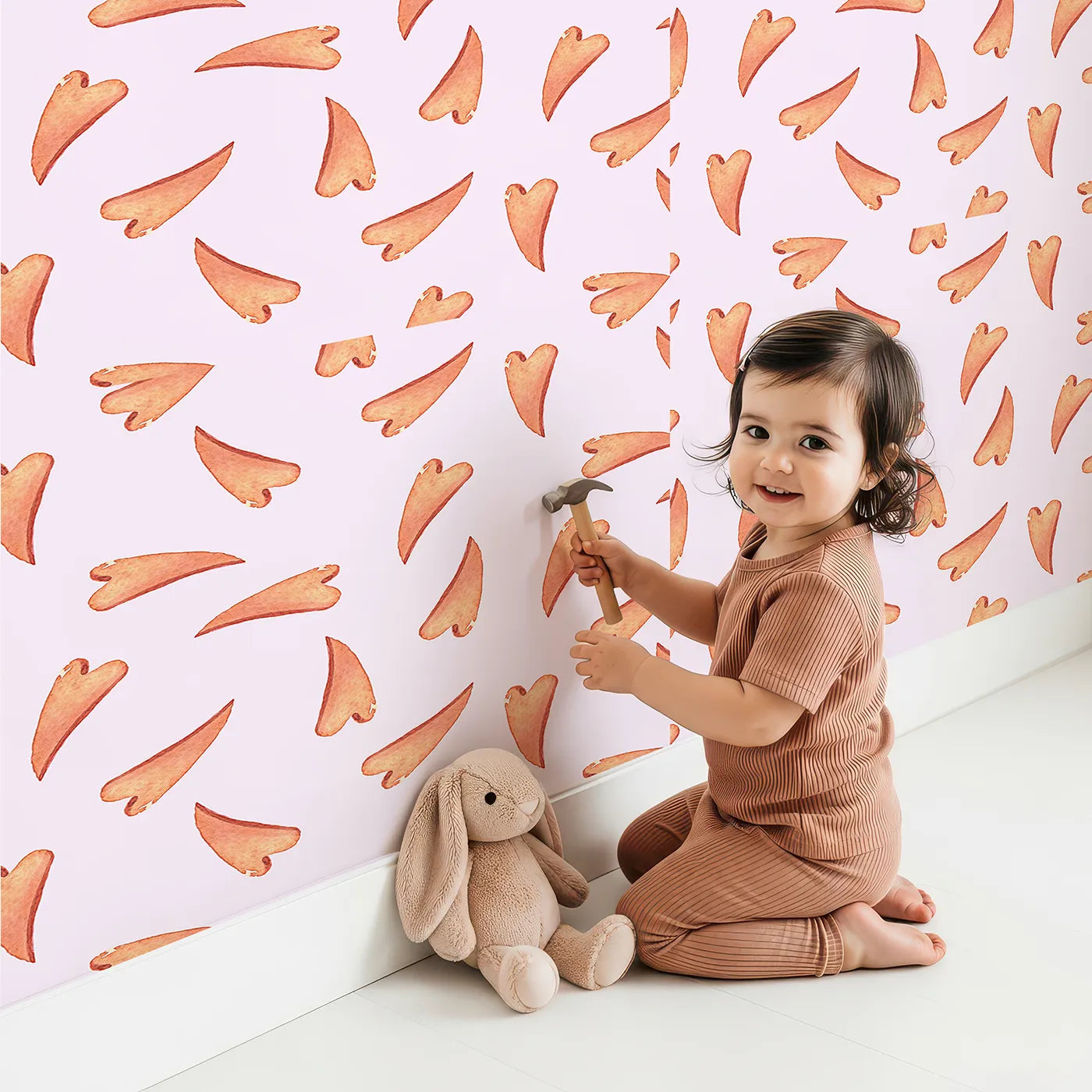 Lovely child standing in front of Whimsy Tots Scattered Heart Sprinkles Wallpaper in Blush with heart, brushstroke, splash in design.
