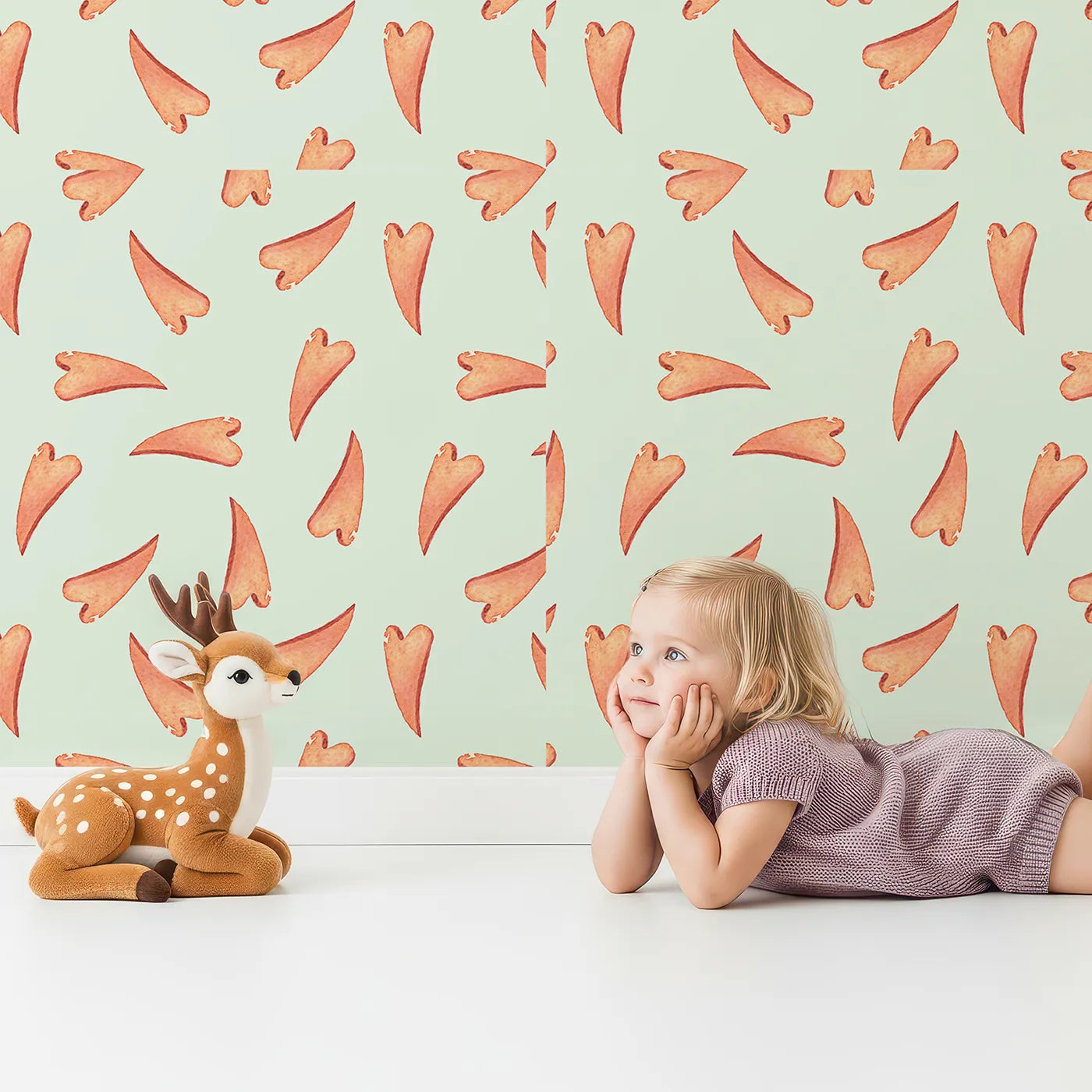 Lovely child standing in front of Whimsy Tots Scattered Heart Sprinkles Wallpaper in Mint with heart, brushstroke, splash in design.