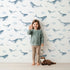 Lovely child standing in front of Whimsy Tots Whale Cloud Voyage Wallpaper in White with whale, cloud, splash in design. Lovely child standing in front of Whimsy Tots Whale Cloud Voyage Wallpaper in White with whale, cloud, splash in design.