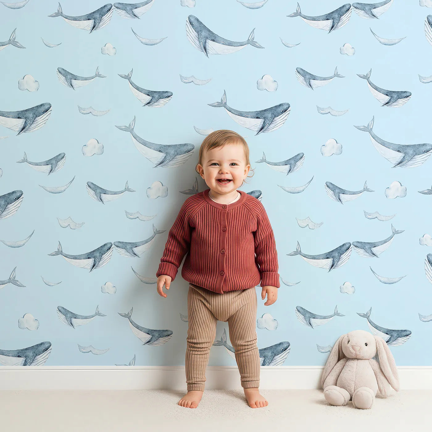 Lovely child standing in front of Whimsy Tots Whale Cloud Voyage Wallpaper in Sky Blue with whale, cloud, splash in design.