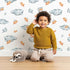 Lovely child standing in front of Whimsy Tots Cloudy Star Drift Wallpaper in White with star, cloud in design. Lovely child standing in front of Whimsy Tots Cloudy Star Drift Wallpaper in White with star, cloud in design.