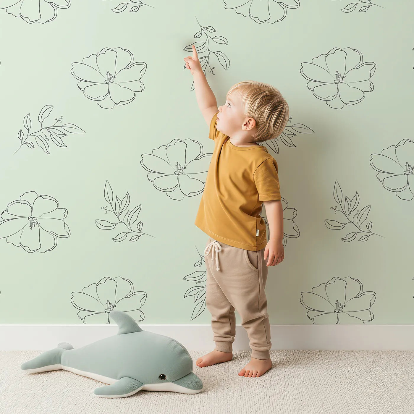 Lovely child standing in front of Whimsy Tots Line Art Camellia Wallpaper in Mint Green with flower, camellia, lineart, leaf in design.