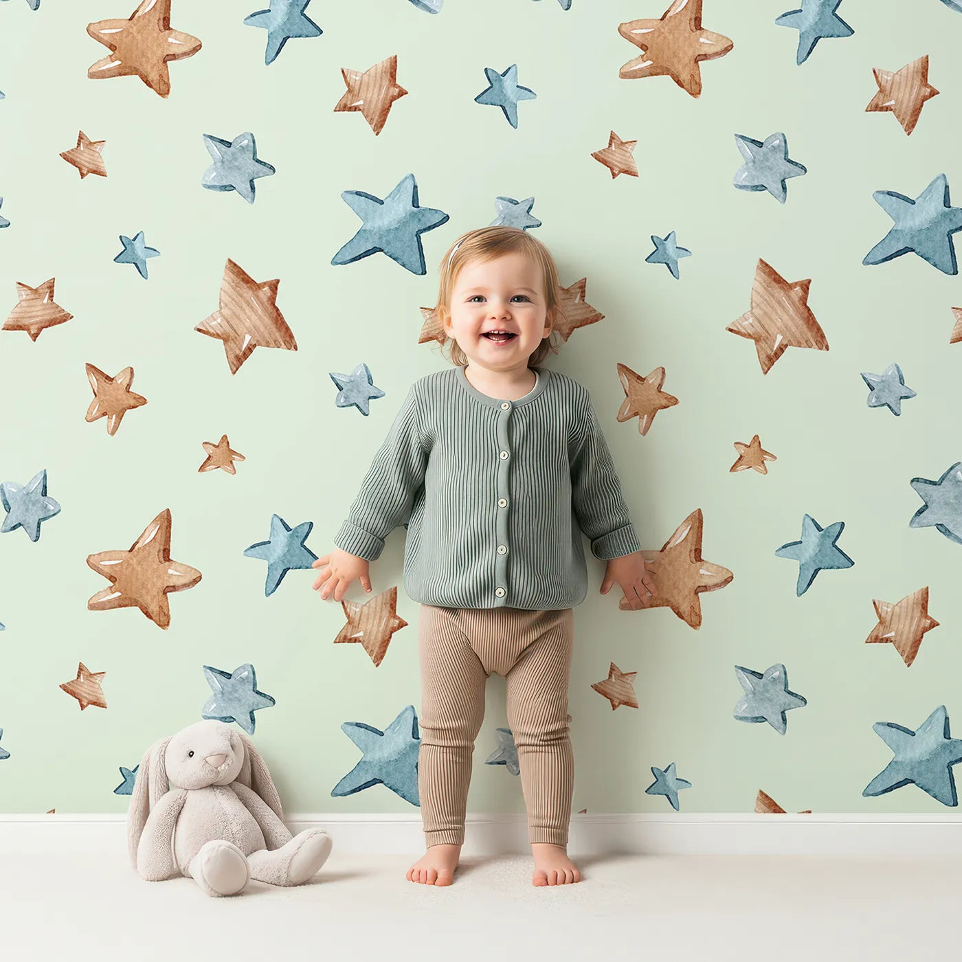 Lovely child standing in front of Whimsy Tots Starry Drift Wallpaper in Mint Green with star, watercolor, sky, night in design.
