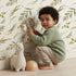 Lovely child standing in front of Whimsy Tots Botanical Breeze Wallpaper in White with leaf, sprig, branch, stem in design. Lovely child standing in front of Whimsy Tots Botanical Breeze Wallpaper in White with leaf, sprig, branch, stem in design.