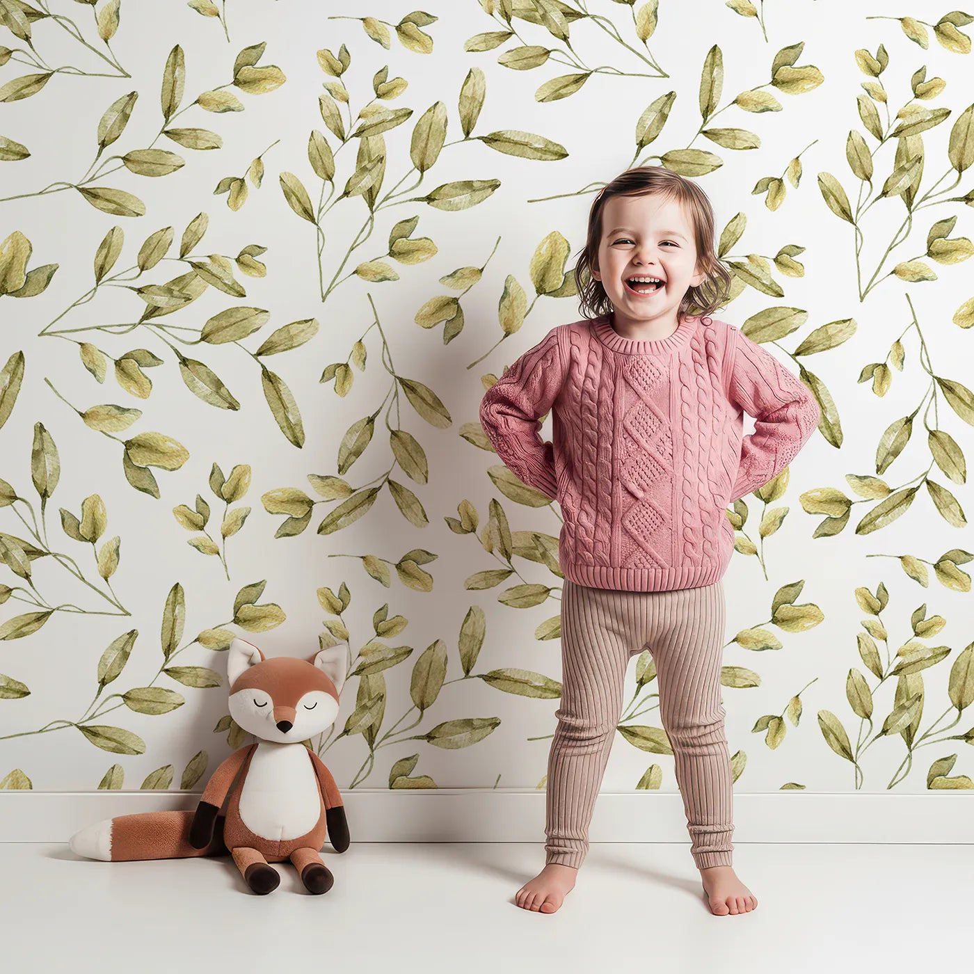 Lovely child standing in front of Whimsy Tots Golden Olive Garden Wallpaper in White with leaf, olive, stem, branch in design.