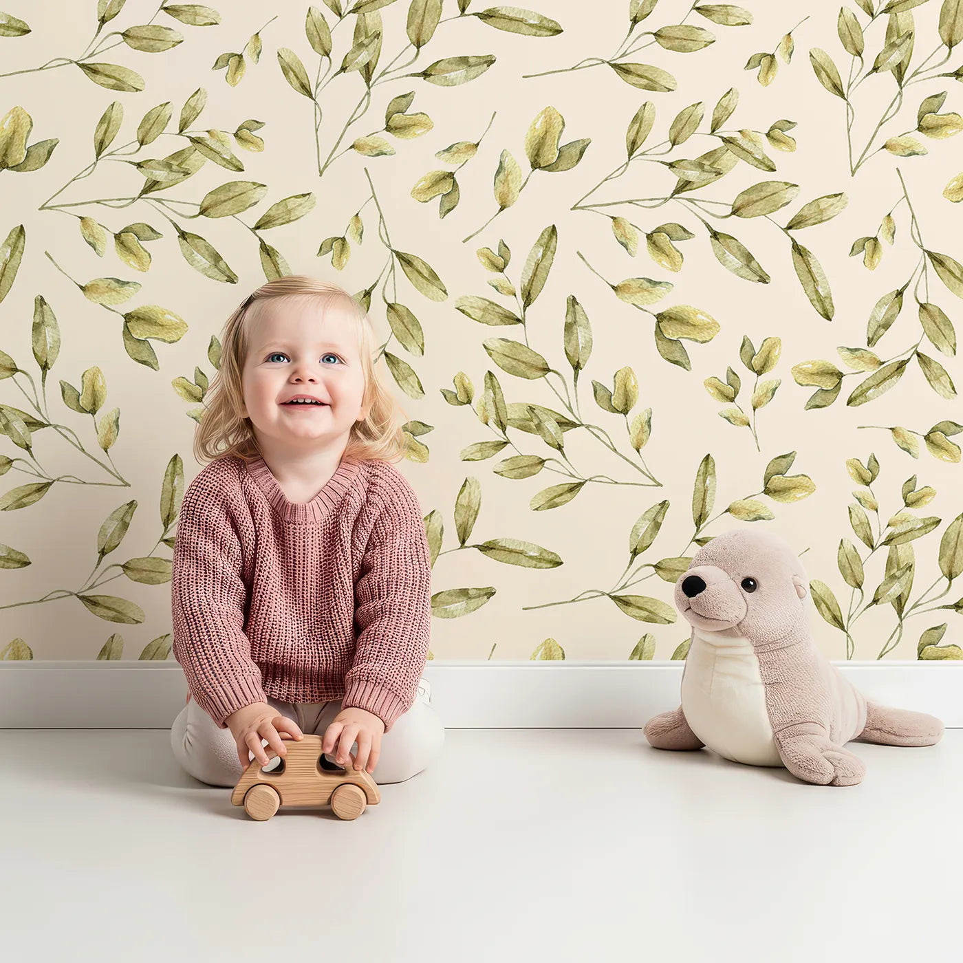 Lovely child standing in front of Whimsy Tots Golden Olive Garden Wallpaper in Cream with leaf, olive, stem, branch in design.