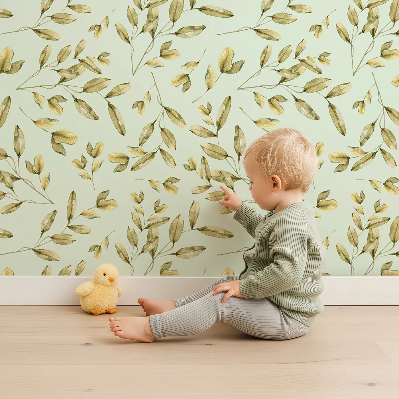 Lovely child standing in front of Whimsy Tots Golden Olive Garden Wallpaper in Mint with leaf, olive, sprig, branch in design.