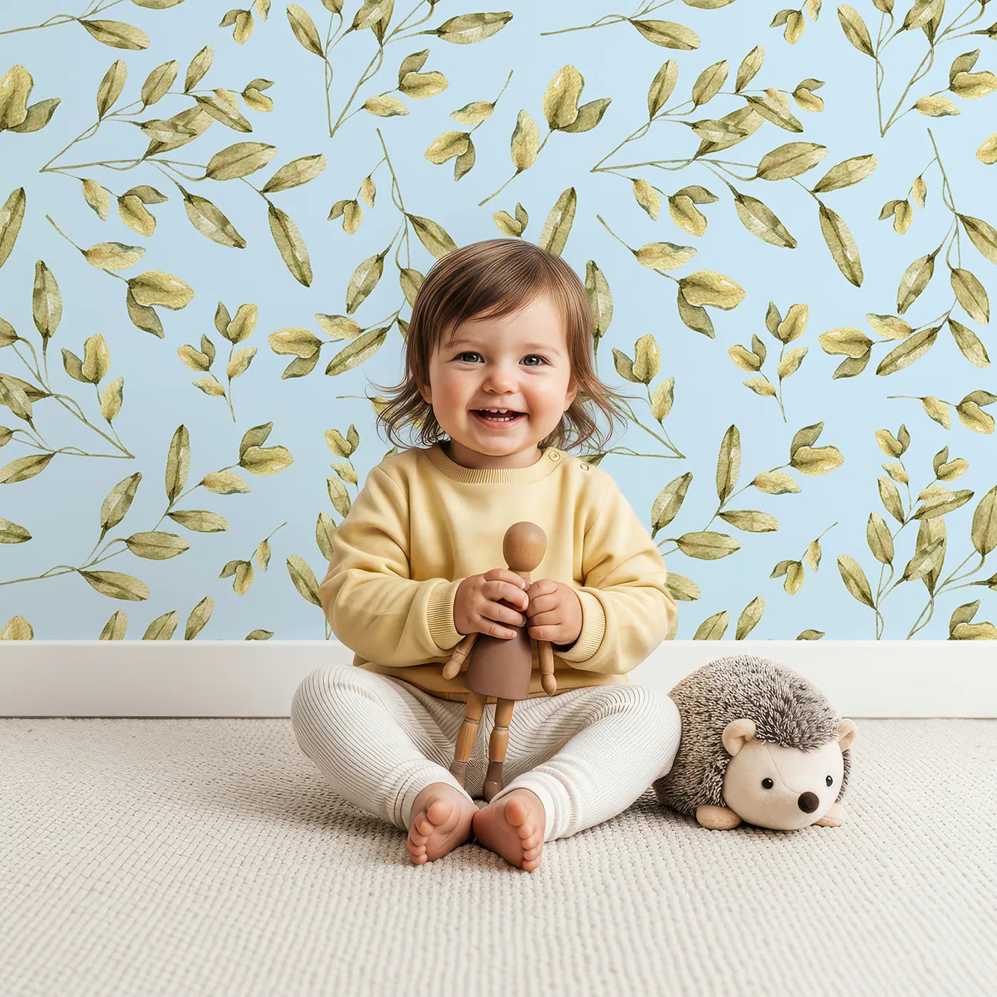 Lovely child standing in front of Whimsy Tots Golden Olive Garden Wallpaper in Sky with leaf, olive, sprig, stem in design.