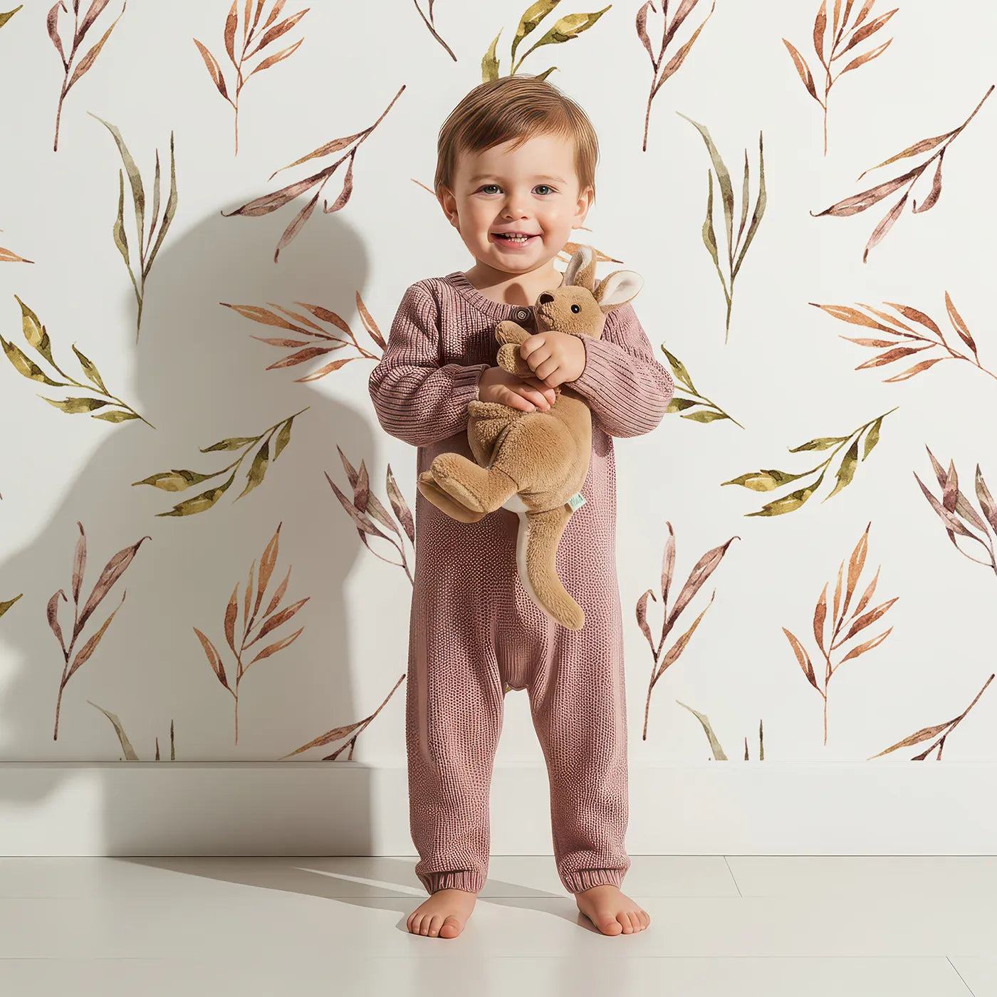Lovely child standing in front of Whimsy Tots Sunset Meadow Breeze Wallpaper in White with leaf, branch, stem in design.