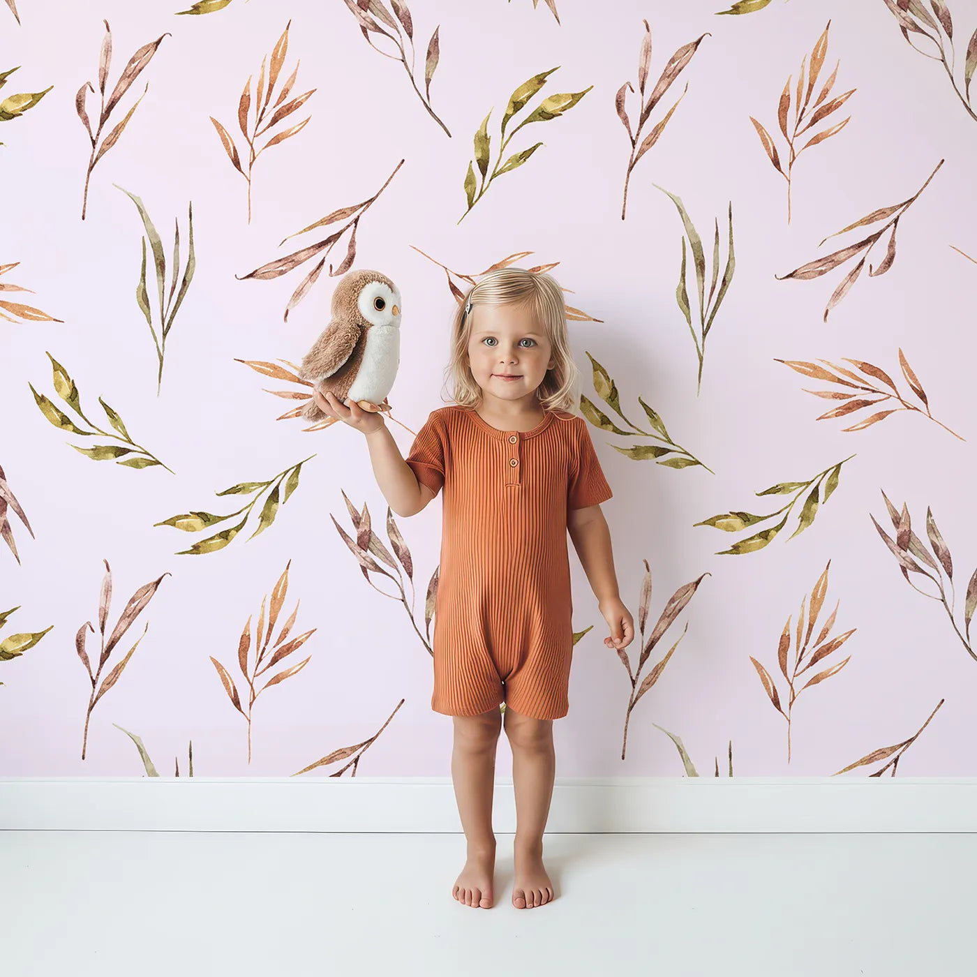 Lovely child standing in front of Whimsy Tots Sunset Meadow Breeze Wallpaper in Blush Pink with leaf, stem, sprig in design.