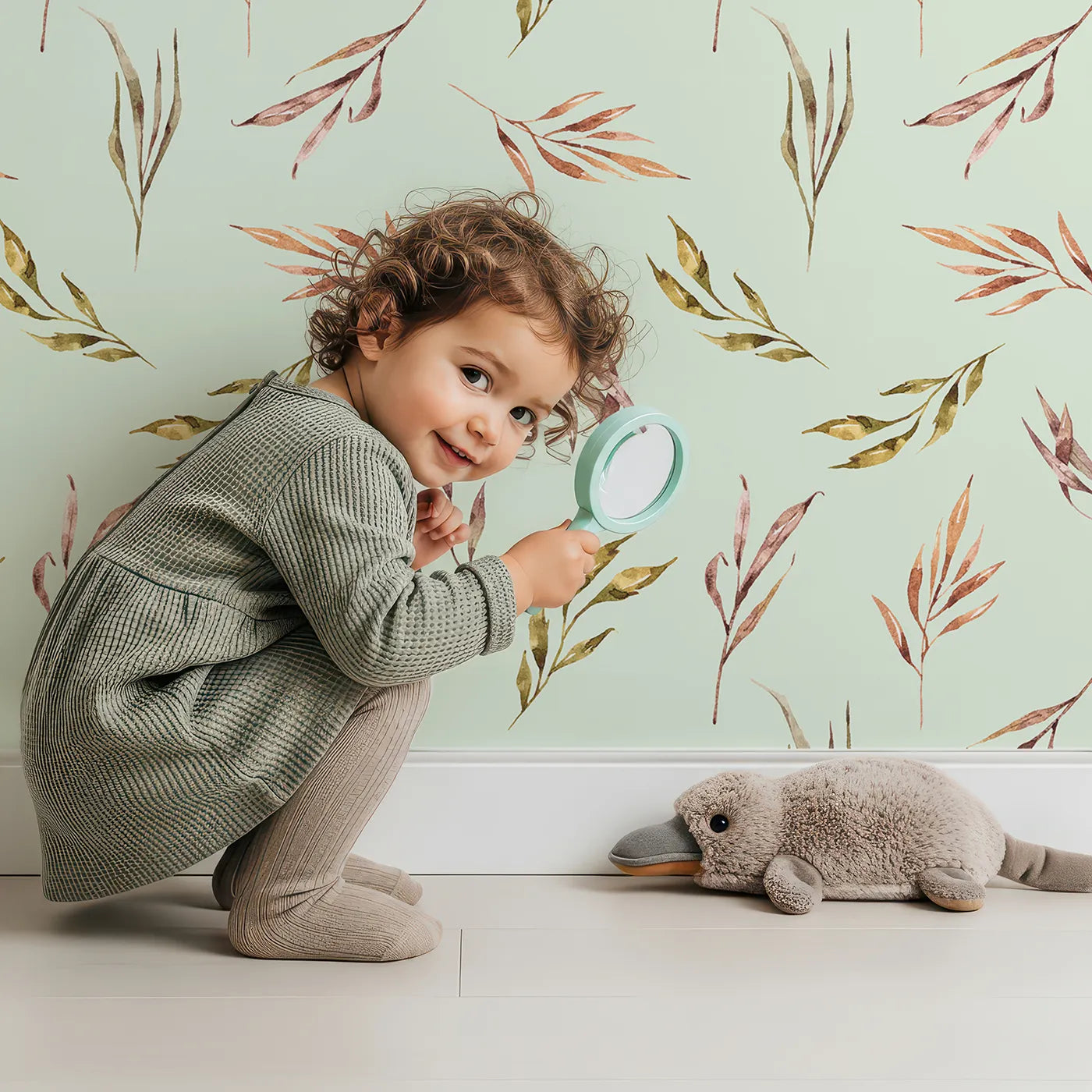 Lovely child standing in front of Whimsy Tots Sunset Meadow Breeze Wallpaper in Mint Green with leaf, stem, sprig in design.
