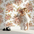 Lovely child standing in front of Whimsy Tots Autumn Bloom Harmony Wallpaper in White with flower, rose, peony, branch in design. Lovely child standing in front of Whimsy Tots Autumn Bloom Harmony Wallpaper in White with flower, rose, peony, branch in design.