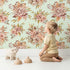 Lovely child standing in front of Whimsy Tots Autumn Bloom Harmony Wallpaper in Mint Green with flower, bouquet, rose, peony in design. Lovely child standing in front of Whimsy Tots Autumn Bloom Harmony Wallpaper in Mint Green with flower, bouquet, rose, peony in design.