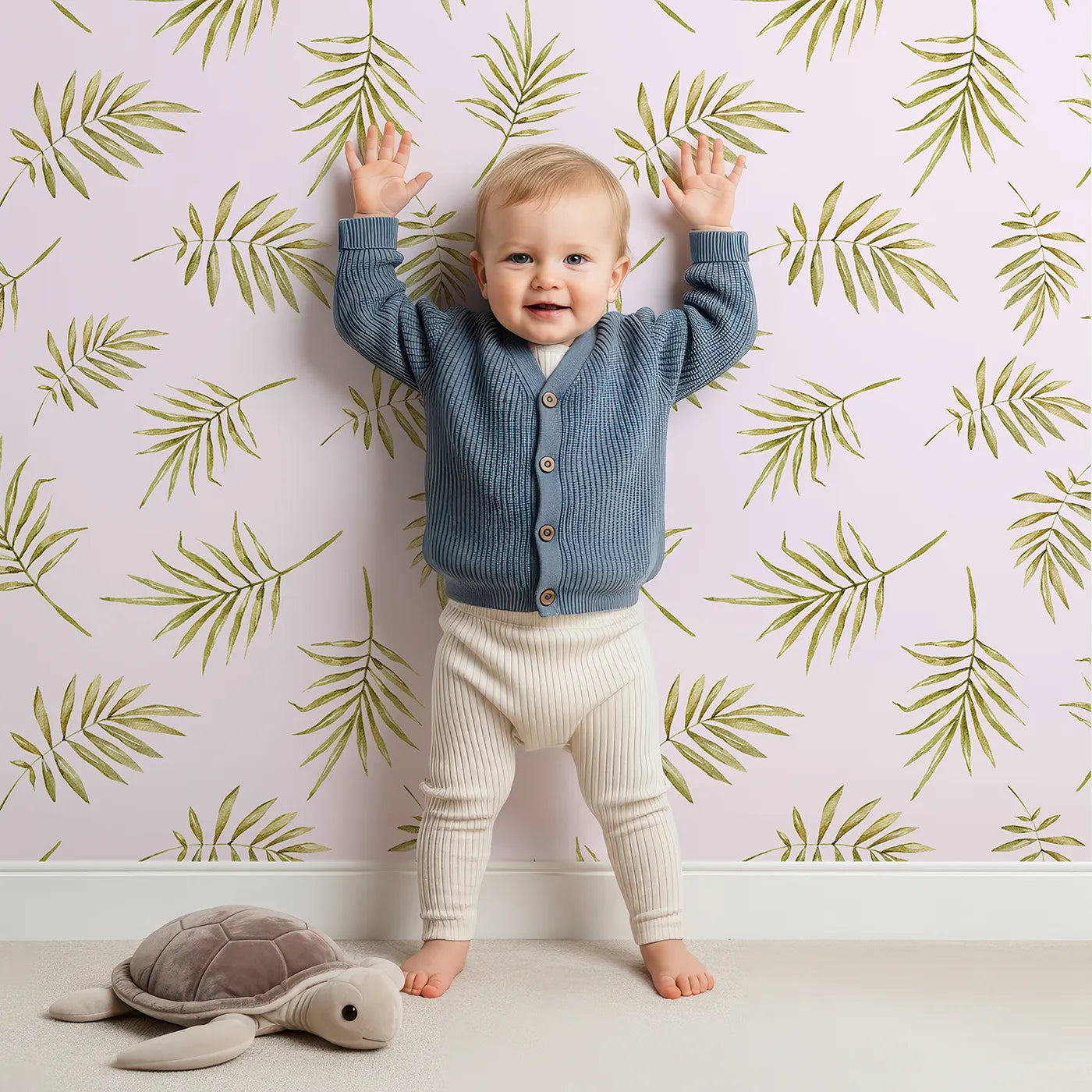 Lovely child standing in front of Whimsy Tots Gentle Palm Scatter Wallpaper in Blush Pink with leaf, palm in design.