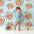 Lovely child standing in front of Whimsy Tots Harvest Bloom Hoop Wallpaper in Blue with flower, pumpkin, hoop, leaf in design. Lovely child standing in front of Whimsy Tots Harvest Bloom Hoop Wallpaper in Blue with flower, pumpkin, hoop, leaf in design.