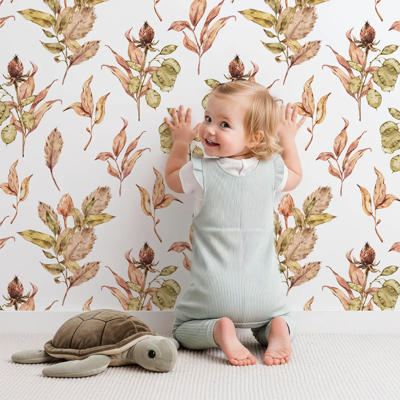 Lovely child standing in front of Whimsy Tots Autumn Forage Garden Wallpaper in White with leaf, pod, sprig, branch in design.