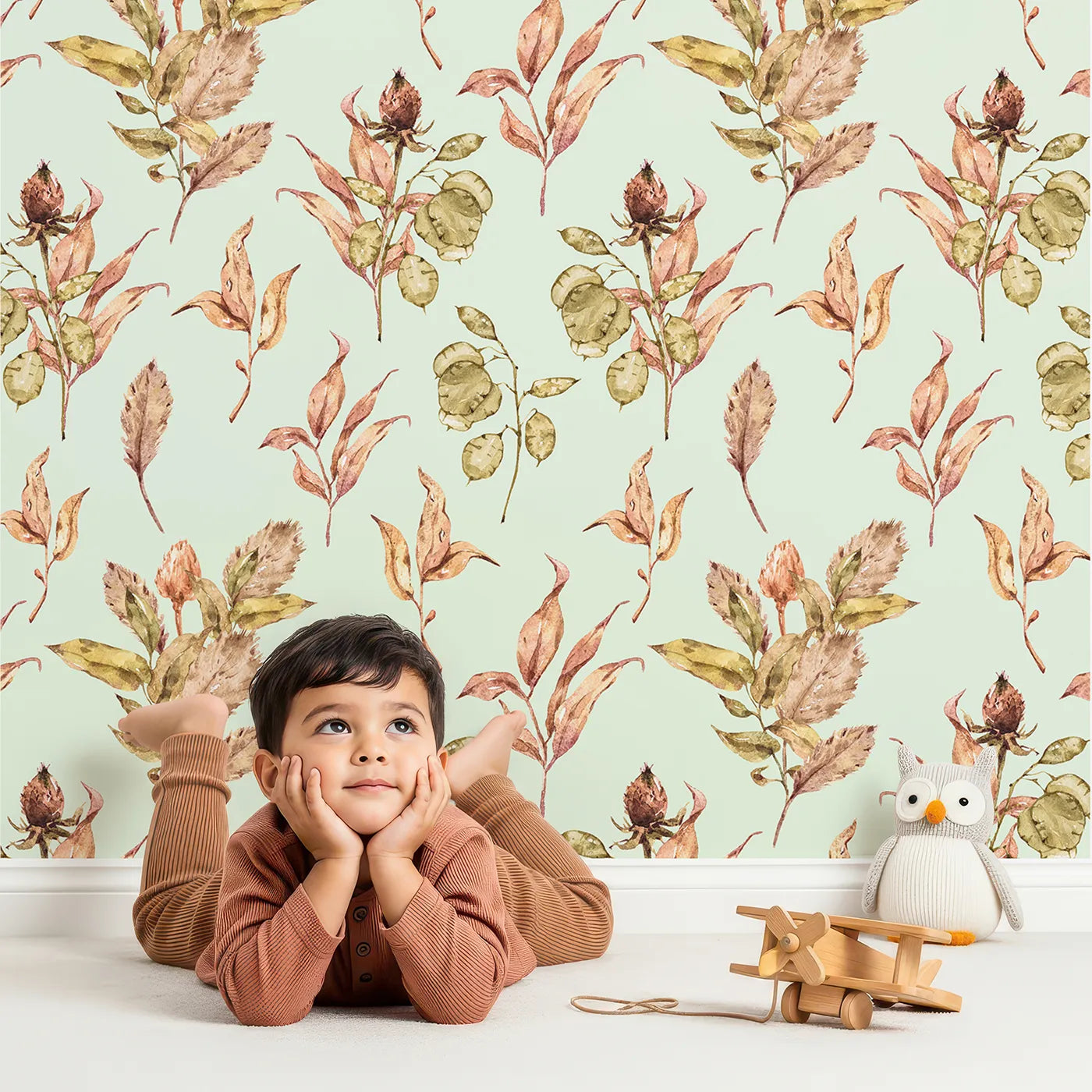 Lovely child standing in front of Whimsy Tots Autumn Forage Garden Wallpaper in Mint Green with leaf, pod, sprig, branch in design.