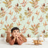 Lovely child standing in front of Whimsy Tots Autumn Forage Garden Wallpaper in Mint Green with leaf, pod, sprig, branch in design. Lovely child standing in front of Whimsy Tots Autumn Forage Garden Wallpaper in Mint Green with leaf, pod, sprig, branch in design.