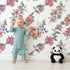 Lovely child standing in front of Whimsy Tots Winter Blooming Garden Wallpaper in White with flower, cotton, eucalyptus, poinsettia in design. Lovely child standing in front of Whimsy Tots Winter Blooming Garden Wallpaper in White with flower, cotton, eucalyptus, poinsettia in design.