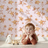 Lovely child standing in front of Whimsy Tots Golden Star Scatter Wallpaper in Blush with star in design. Lovely child standing in front of Whimsy Tots Golden Star Scatter Wallpaper in Blush with star in design.