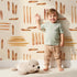 Lovely child standing in front of Whimsy Tots Painted Rhythm Wallpaper in Cream with line, brushstroke in design. Lovely child standing in front of Whimsy Tots Painted Rhythm Wallpaper in Cream with line, brushstroke in design.