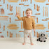 Lovely child standing in front of Whimsy Tots Painted Rhythm Wallpaper in Sky Blue with line, brushstroke in design. Lovely child standing in front of Whimsy Tots Painted Rhythm Wallpaper in Sky Blue with line, brushstroke in design.