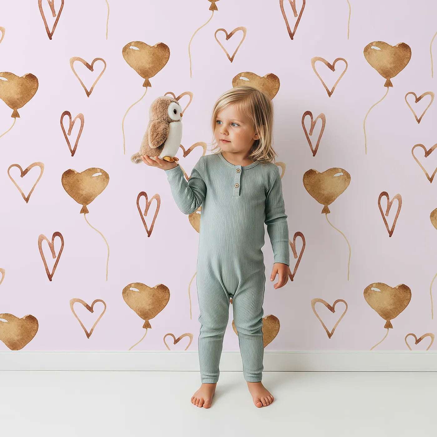 Lovely child standing in front of Whimsy Tots Heartfelt Balloons Wallpaper in Pink with heart, balloon, outline in design.