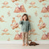 Lovely child standing in front of Whimsy Tots Feathered Serenity Wallpaper in Mint with bird, swan, crown, mountain, wing in design. Lovely child standing in front of Whimsy Tots Feathered Serenity Wallpaper in Mint with bird, swan, crown, mountain, wing in design.