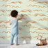 Lovely child standing in front of Whimsy Tots Soft Wave Rhythm Wallpaper in Mint Green with wave, curve, line, brushstroke, abstract in design. Lovely child standing in front of Whimsy Tots Soft Wave Rhythm Wallpaper in Mint Green with wave, curve, line, brushstroke, abstract in design.