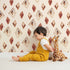 Lovely child standing in front of Whimsy Tots Terracotta Diamond Dance Wallpaper in Sand with diamond, shape, rust, abstract, terracotta in design. Lovely child standing in front of Whimsy Tots Terracotta Diamond Dance Wallpaper in Sand with diamond, shape, rust, abstract, terracotta in design.