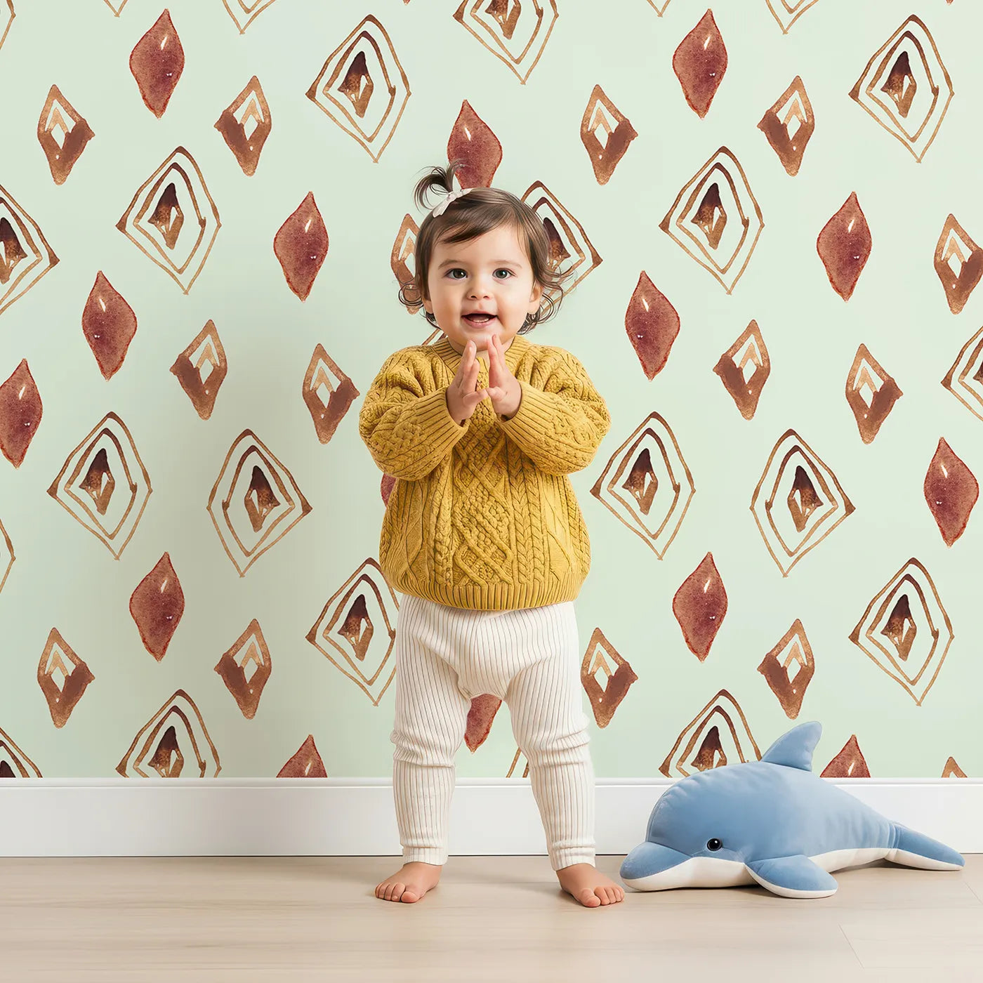 Lovely child standing in front of Whimsy Tots Terracotta Diamond Dance Wallpaper in Mint Green with diamond, shape, rust, abstract, terracotta in design.