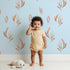 Lovely child standing in front of Whimsy Tots Rustling Meadow Sprigs Wallpaper in Sky with leaf, sprig, botanical, plant in design. Lovely child standing in front of Whimsy Tots Rustling Meadow Sprigs Wallpaper in Sky with leaf, sprig, botanical, plant in design.
