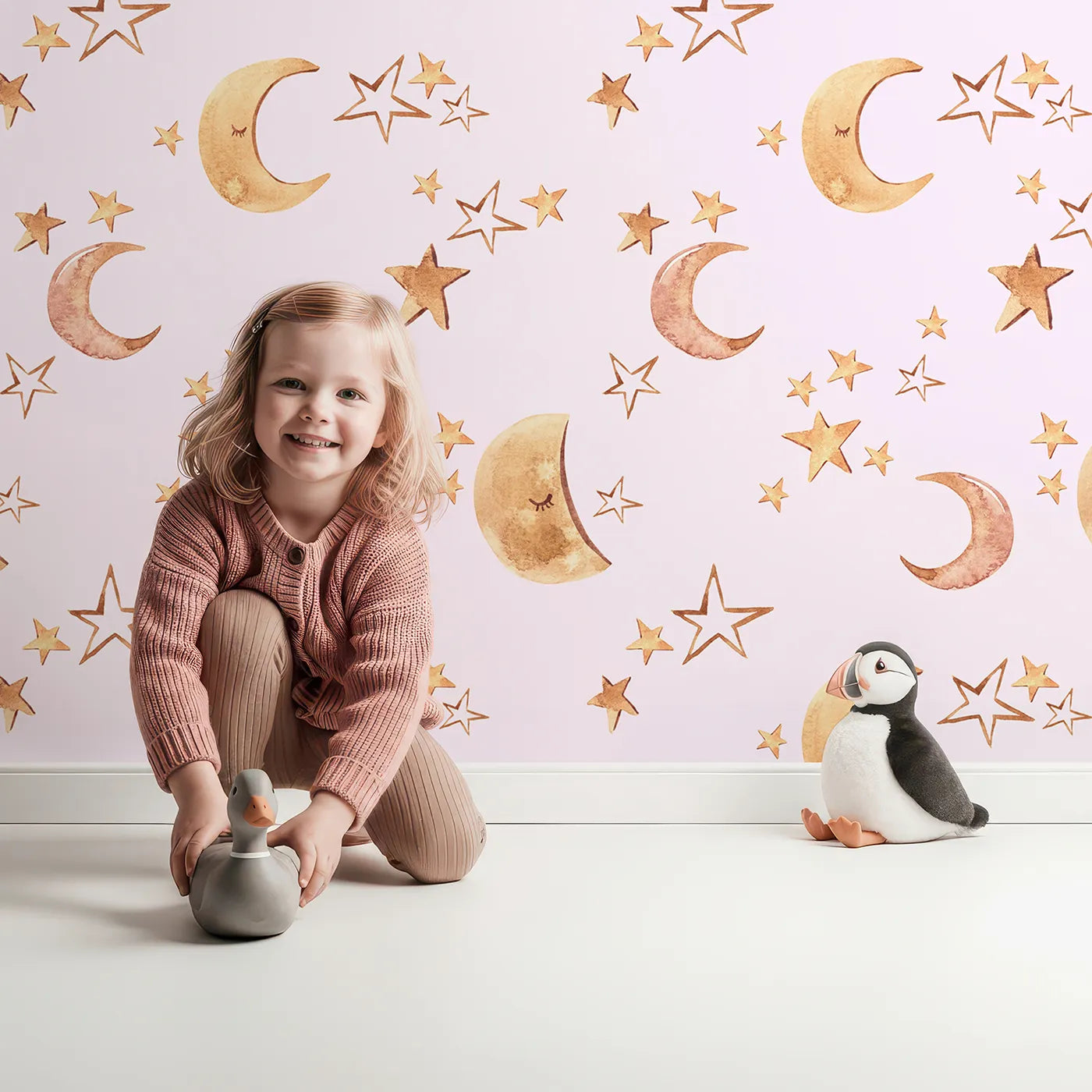 Lovely child standing in front of Whimsy Tots Sleepy Skies Shine Wallpaper in Blush Pink with moon, star, sky, sleepy face in design.