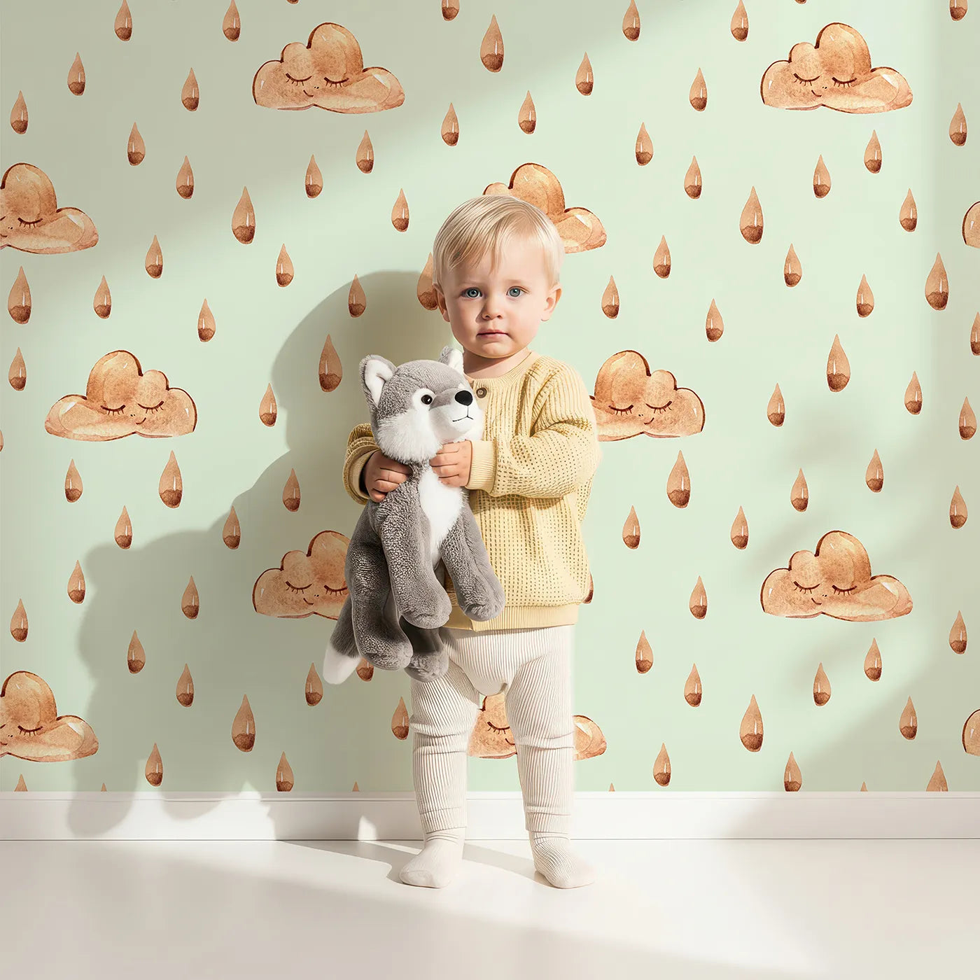 Lovely child standing in front of Whimsy Tots Rainy Day Nap Wallpaper in Mint Green with cloud, raindrop, sleepy face in design.