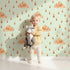 Lovely child standing in front of Whimsy Tots Rainy Day Nap Wallpaper in Mint Green with cloud, raindrop, sleepy face in design. Lovely child standing in front of Whimsy Tots Rainy Day Nap Wallpaper in Mint Green with cloud, raindrop, sleepy face in design.