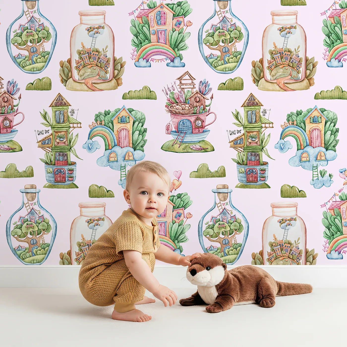 Lovely child standing in front of Whimsy Tots Whimsy Village Dreams Wallpaper in Blush Pink with house, rainbow, cup, jar, cloud, balloon in design.
