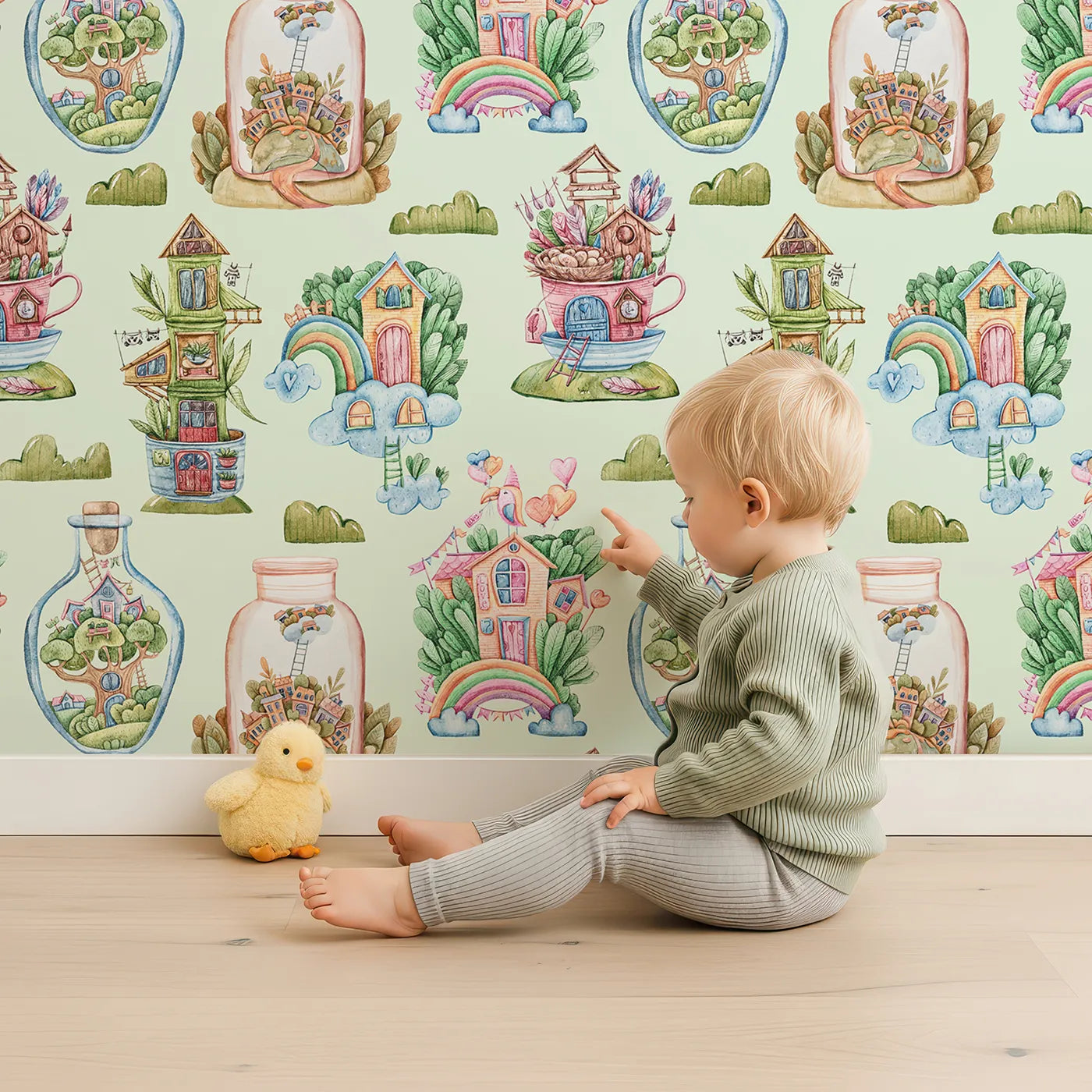 Lovely child standing in front of Whimsy Tots Whimsy Village Dreams Wallpaper in Mint Green with house, rainbow, cup, jar, cloud, balloon in design.