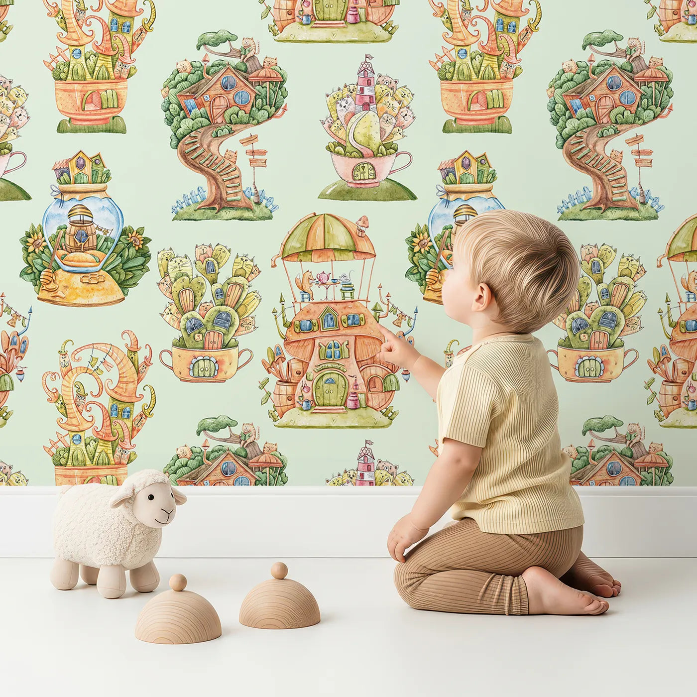 Lovely child standing in front of Whimsy Tots Curious Critter Village Wallpaper in Green with house, cat, tree, cup, ladder, jar, tower in design.