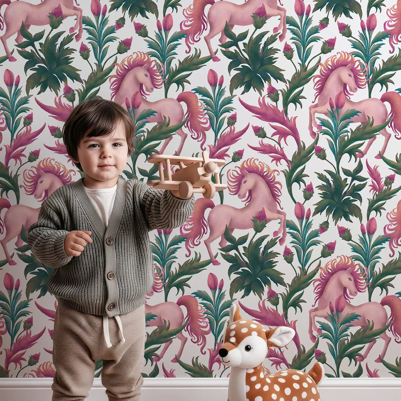 Lovely child standing in front of Whimsy Tots Enchanted Meadow Prance Wallpaper in White with unicorn, flower, leaf, tulip in design.