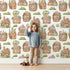 Lovely child standing in front of Whimsy Tots Secret Garden Cutaway Homes Wallpaper in White with house, mushroom, tree, root, gourd, vegetable in design. Lovely child standing in front of Whimsy Tots Secret Garden Cutaway Homes Wallpaper in White with house, mushroom, tree, root, gourd, vegetable in design.