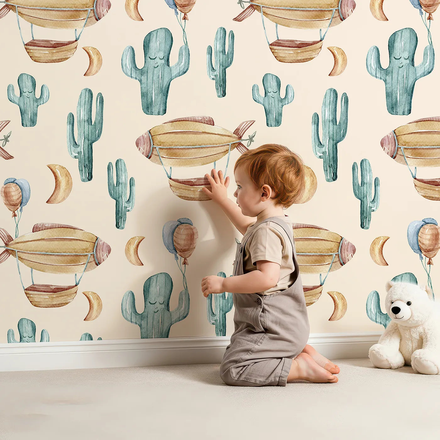 Lovely child standing in front of Whimsy Tots Cactus Cloud Voyage Wallpaper in Sand with cactus, airship, balloon, moon in design.