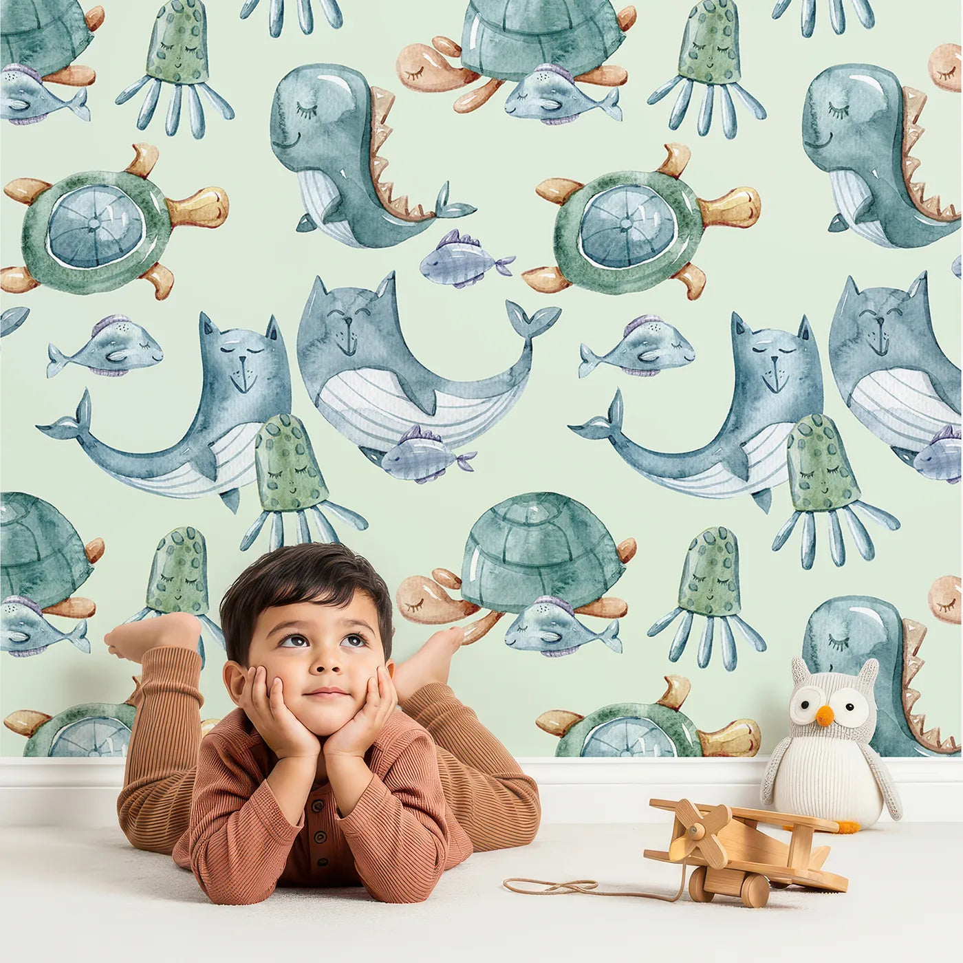 Lovely child standing in front of Whimsy Tots Ocean Pals Parade Wallpaper in Sage Green with whale, turtle, fish, octopus, jellyfish, sea dragon in design.