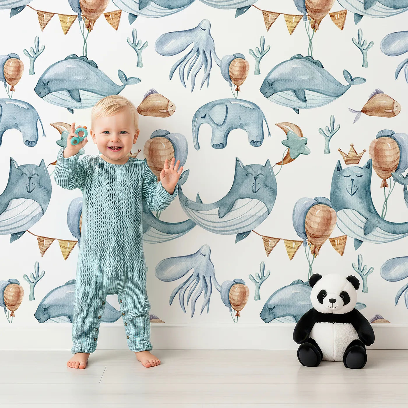 Lovely child standing in front of Whimsy Tots Ocean Pals Celebration Wallpaper in White with whale, balloon, octopus, coral, bunting in design.