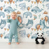 Lovely child standing in front of Whimsy Tots Ocean Pals Celebration Wallpaper in White with whale, balloon, octopus, coral, bunting in design. Lovely child standing in front of Whimsy Tots Ocean Pals Celebration Wallpaper in White with whale, balloon, octopus, coral, bunting in design.