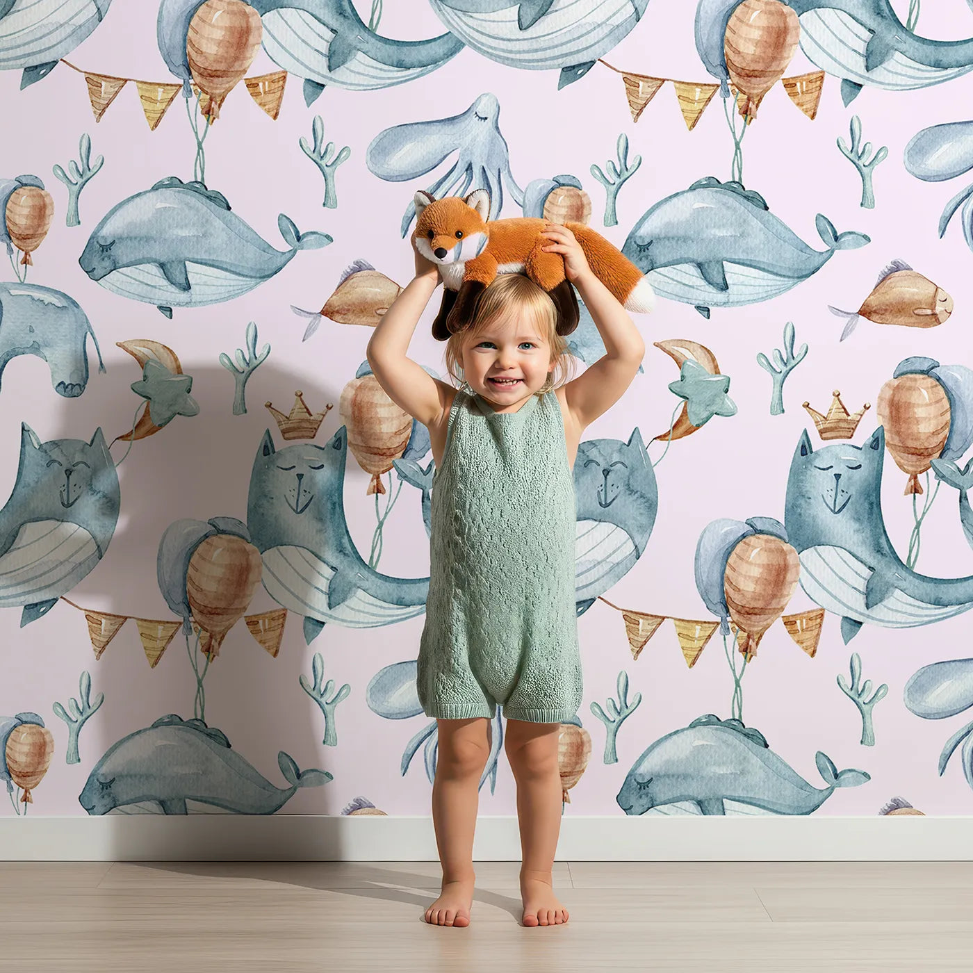 Lovely child standing in front of Whimsy Tots Ocean Pals Celebration Wallpaper in Blush Pink with whale, balloon, octopus, coral, bunting in design.