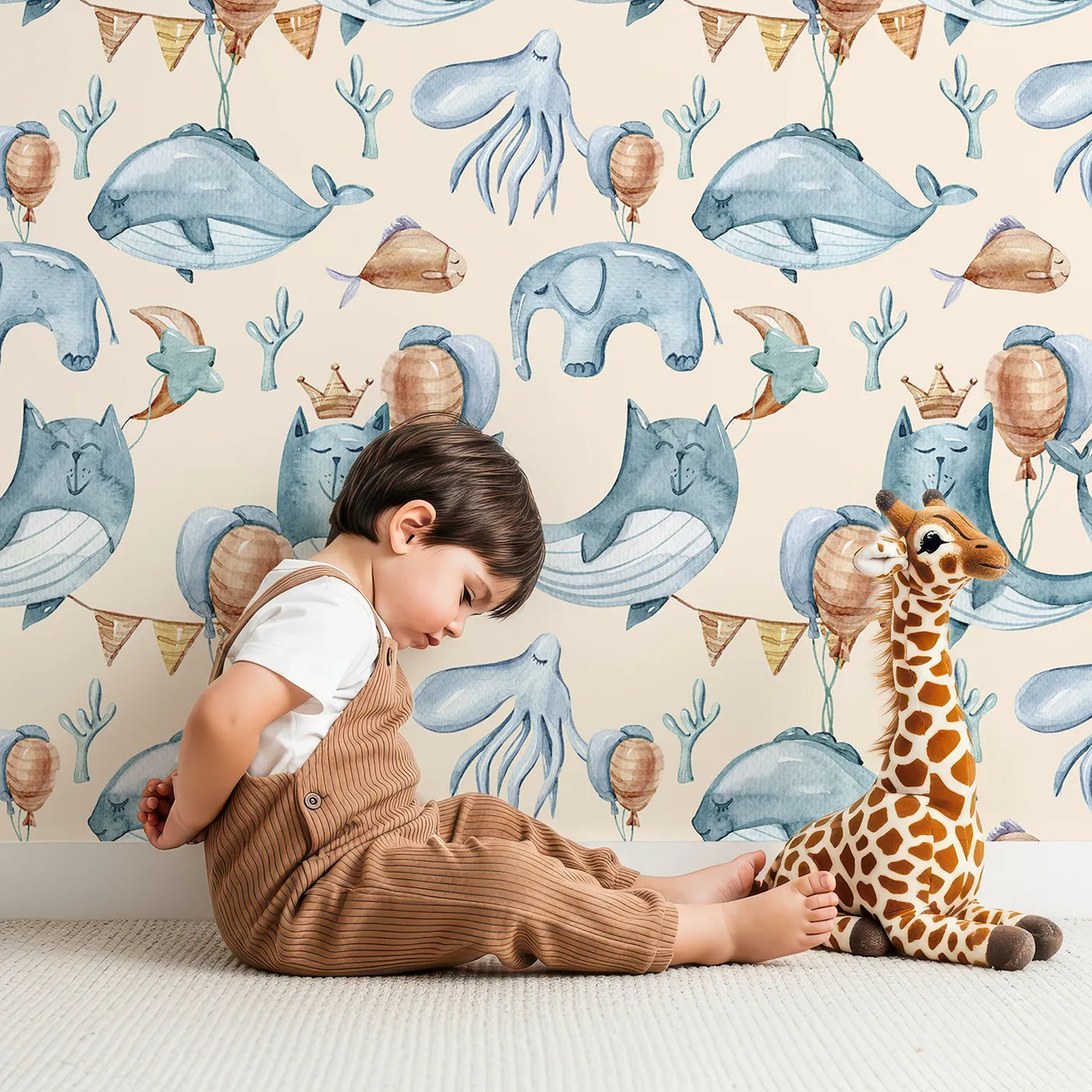 Lovely child standing in front of Whimsy Tots Ocean Pals Celebration Wallpaper in Cream with whale, balloon, octopus, coral, bunting in design.