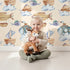 Lovely child standing in front of Whimsy Tots Skybound Explorers Wallpaper in Cream with submarine, boat, fish, cloud, airship in design. Lovely child standing in front of Whimsy Tots Skybound Explorers Wallpaper in Cream with submarine, boat, fish, cloud, airship in design.